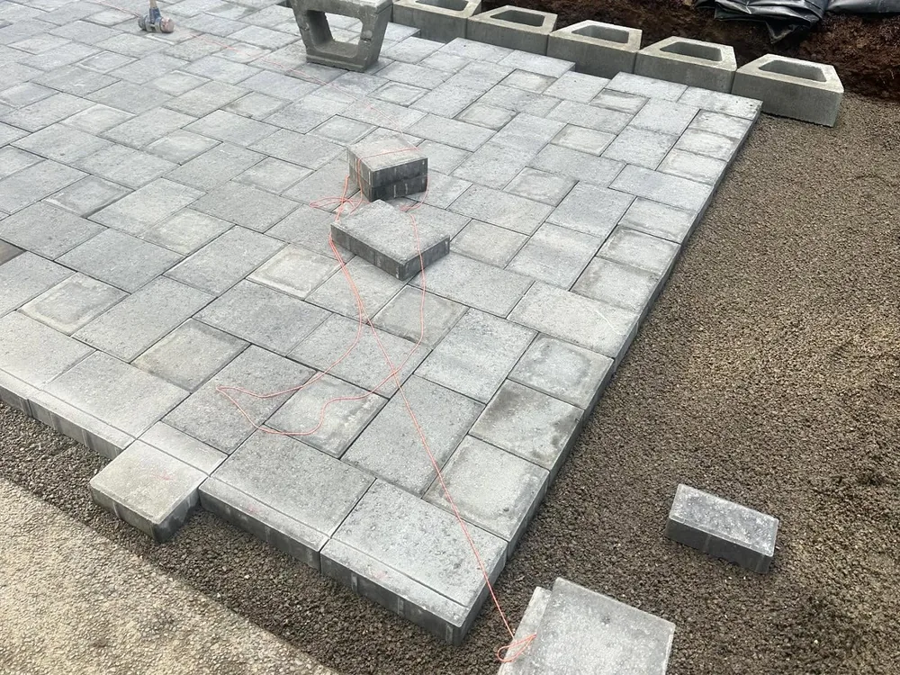 Paver patio in progress: pavers being laid on a prepared base with a string line, beside a row of wall blocks