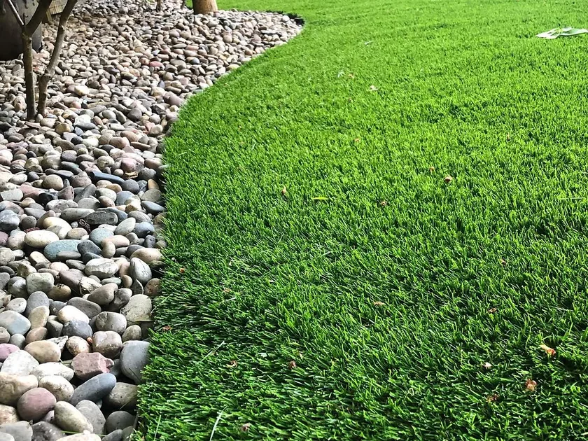 Artificial turf: the finished edge of a synthetic turf lawn against a river rock border