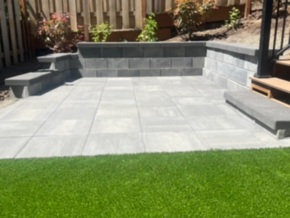 Artificial turf: a synthetic turf lawn in front of a large-format paver patio with a block seat wall and steps