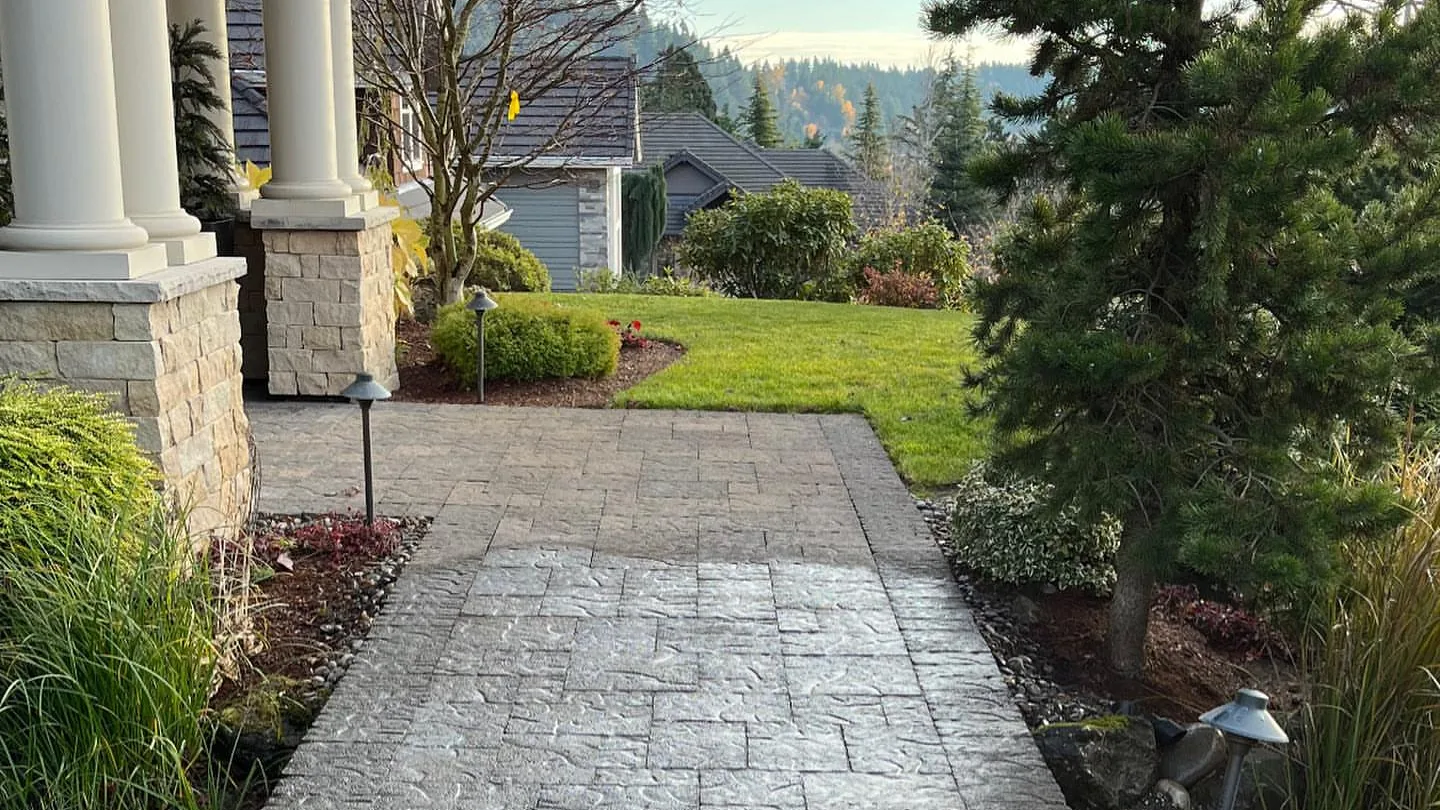 Paver walkway with path lights running from a front porch past a lawn and planting beds