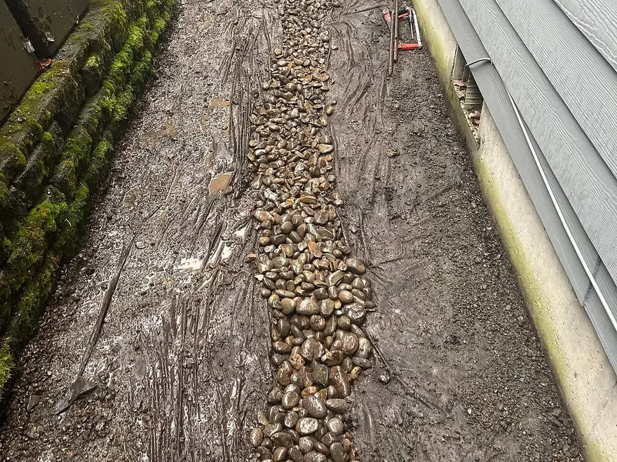 French drains: river rock filling a drain trench along the side of a house