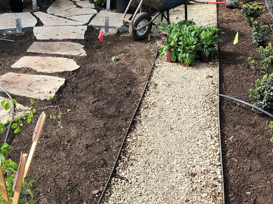 Landscape installation: a yard makeover in progress with flagstone steppers, a gravel path with metal edging and potted plants waiting to go in