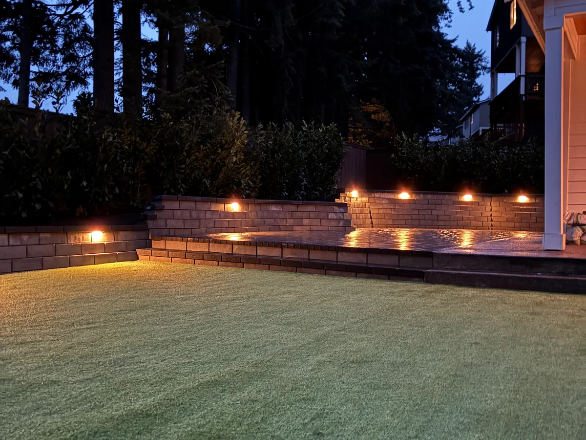 Landscape lighting: lights built into a block seat wall glowing at dusk beside a lawn