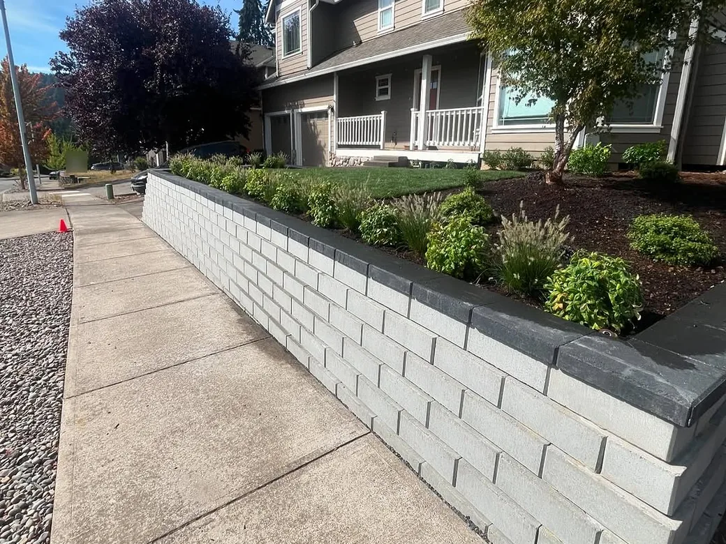 Retaining walls: a segmental block wall with a dark cap holding a new planting bed along a sidewalk