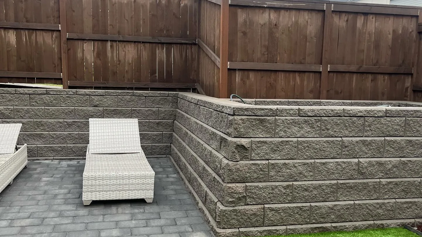 Segmental block retaining wall around a paver patio with artificial turf inside a cedar fence