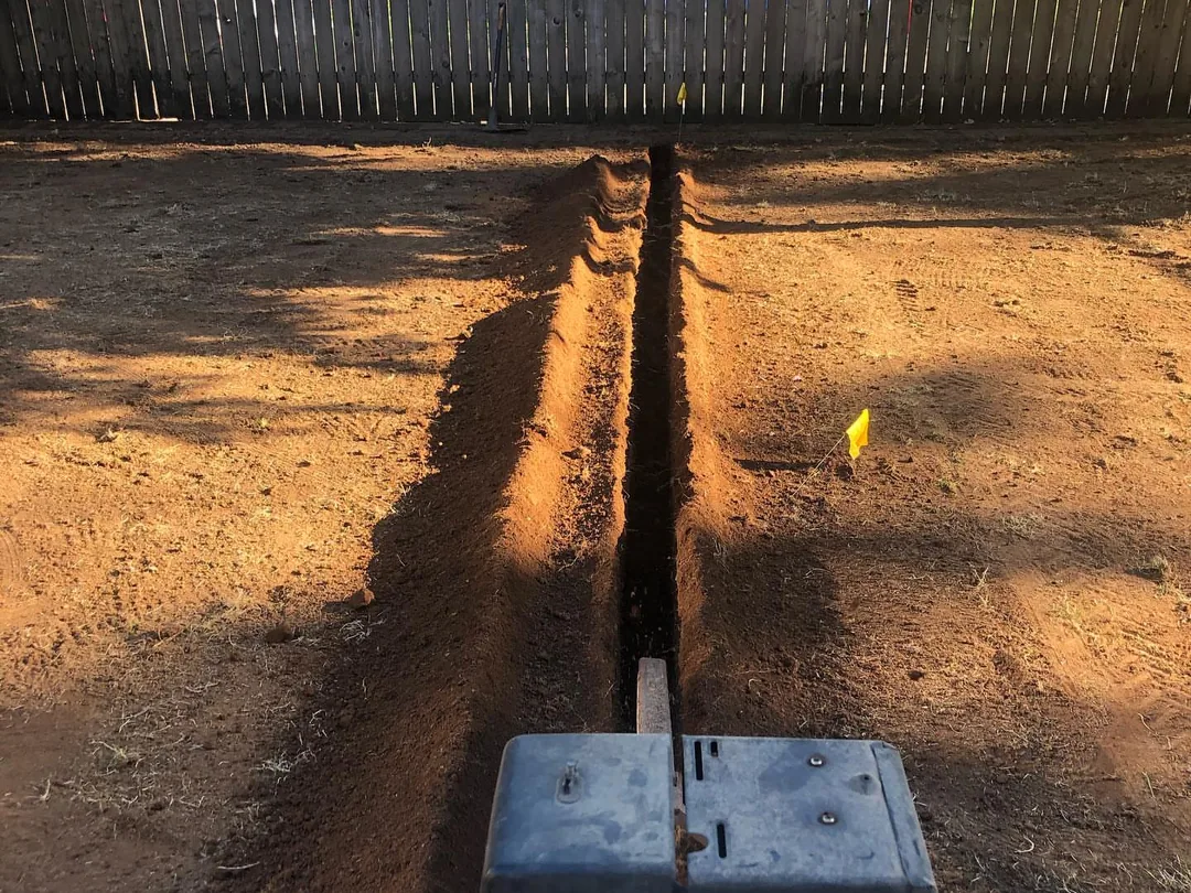 Sprinkler systems: a trencher cutting a narrow trench across a graded yard for new sprinkler lines